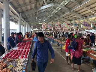 Vendors and shoppers among tables of fresh produce inside Alotau Town Market
