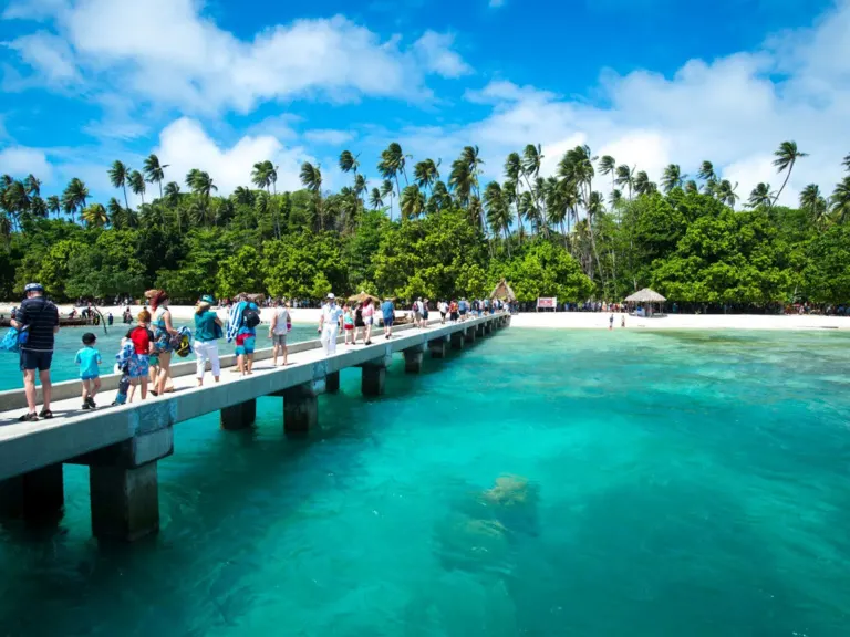 Visitors walking along Kiriwina’s jetty towards a palm-lined beach in the Trobriand Islands