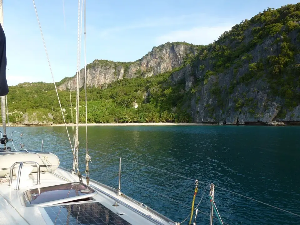 A yacht at anchor beside the forested limestone cliffs of Panasia Island in the Louisiades